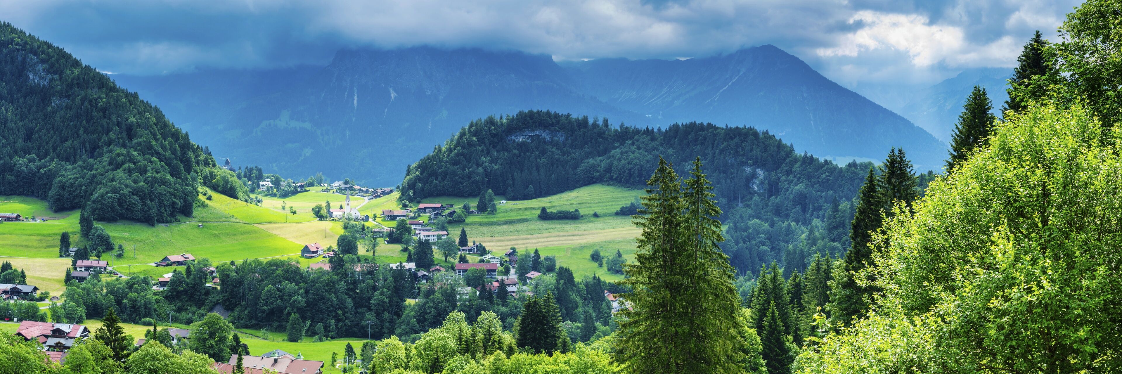A mountainous landscape with a village nestled among green fields and dense forests.