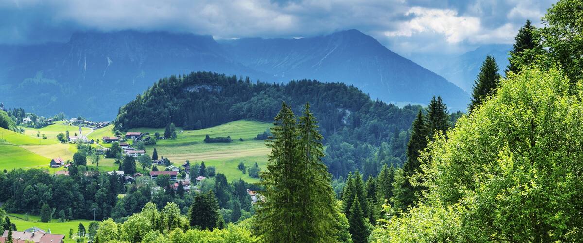 A mountainous landscape with a village nestled among green fields and dense forests.