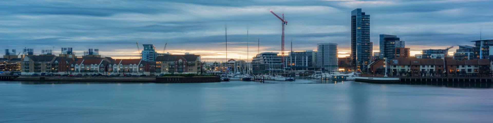 A waterfront cityscape with a marina, buildings, and a crane.