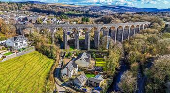 A stone viaduct over a river, surrounded by residential houses and fields.