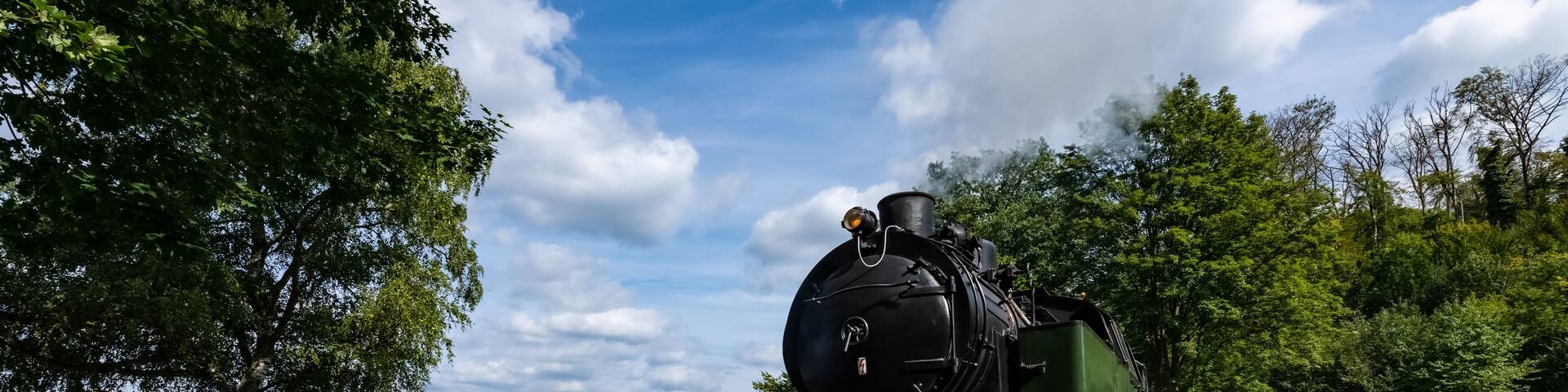 A steam locomotive on tracks by a lake with a sailboat in the distance.