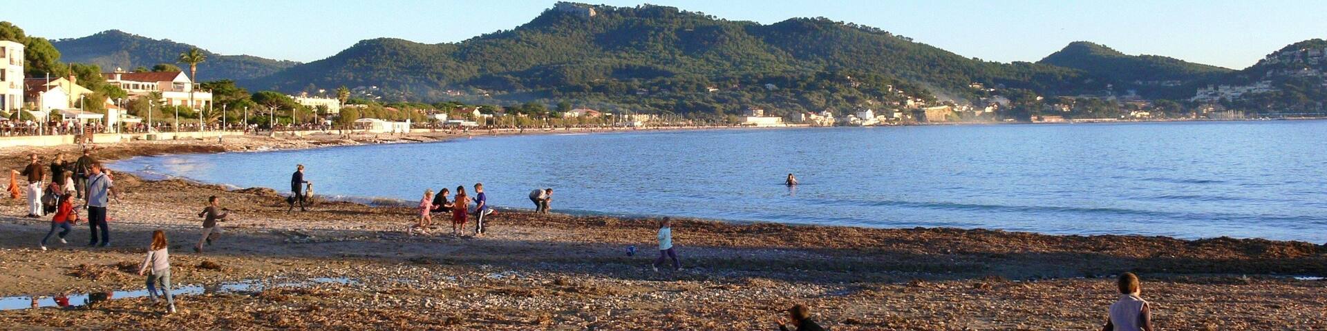 A beach with people playing and walking, a clear sky, and hills in the background.