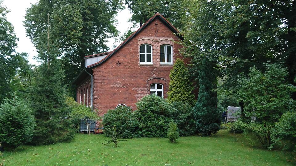 A red brick house surrounded by dense trees and a well-maintained lawn.