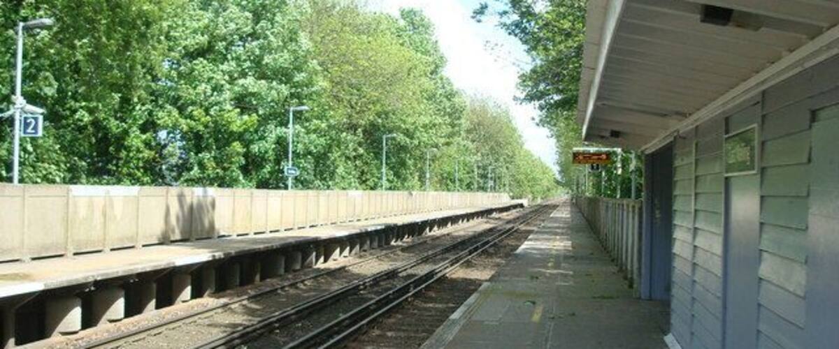 A train station platform with tracks, a shelter, and trees in the background.