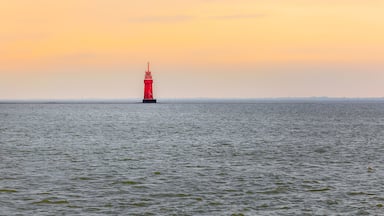 Um farol vermelho em um mar calmo ao pôr do sol.