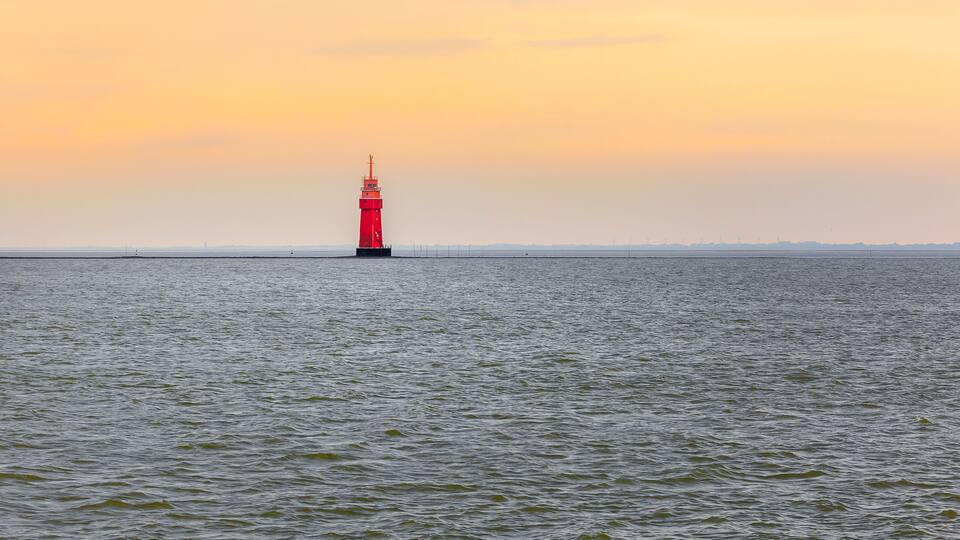 A red lighthouse on a calm sea at sunset.