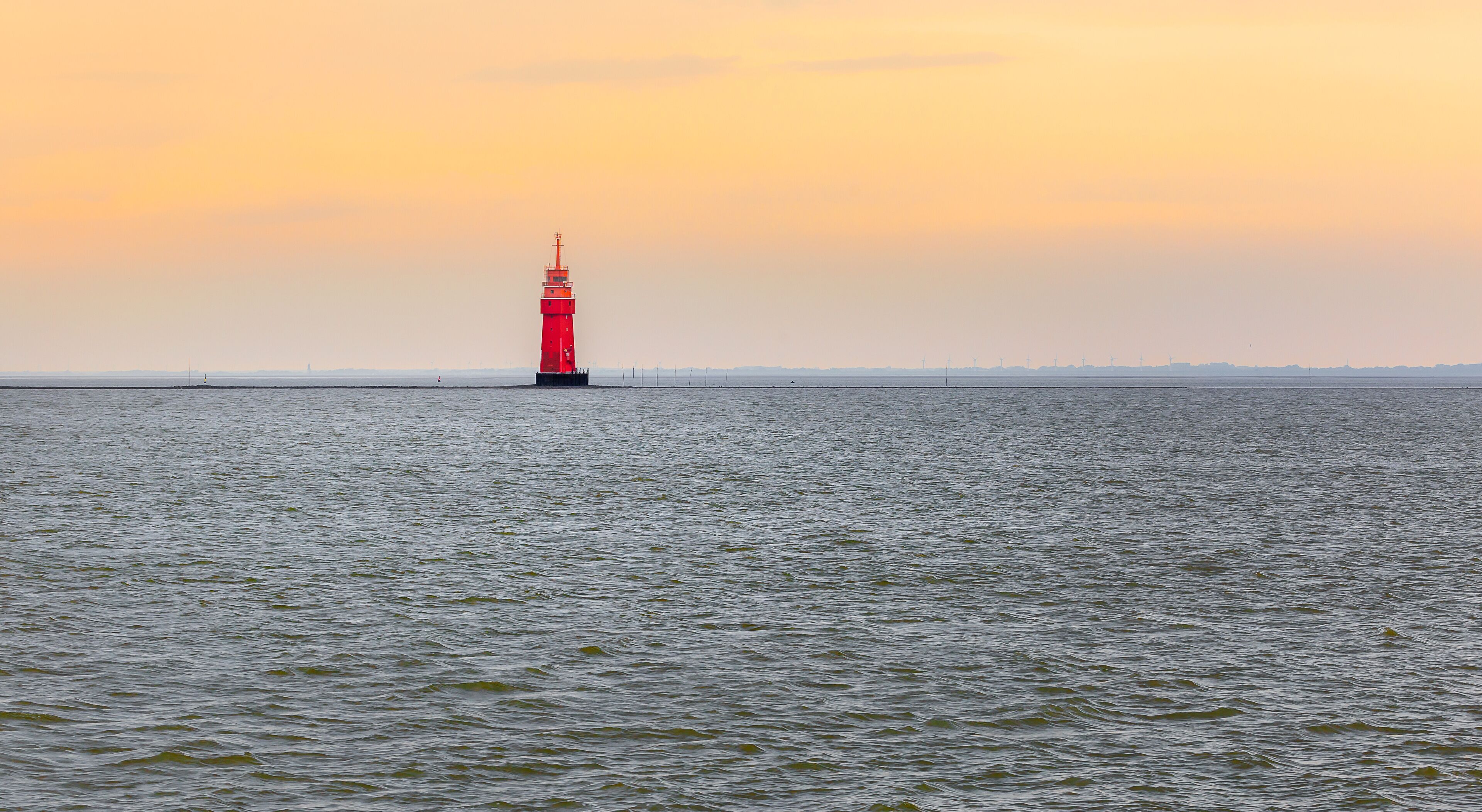 A red lighthouse on a calm sea at sunset.