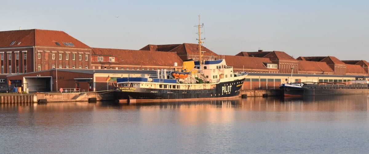 A harbor with a large ship named "Kapitan Konio" docked.