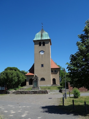 Una iglesia histórica con una torre de reloj, rodeada de vegetación y un camino empedrado.