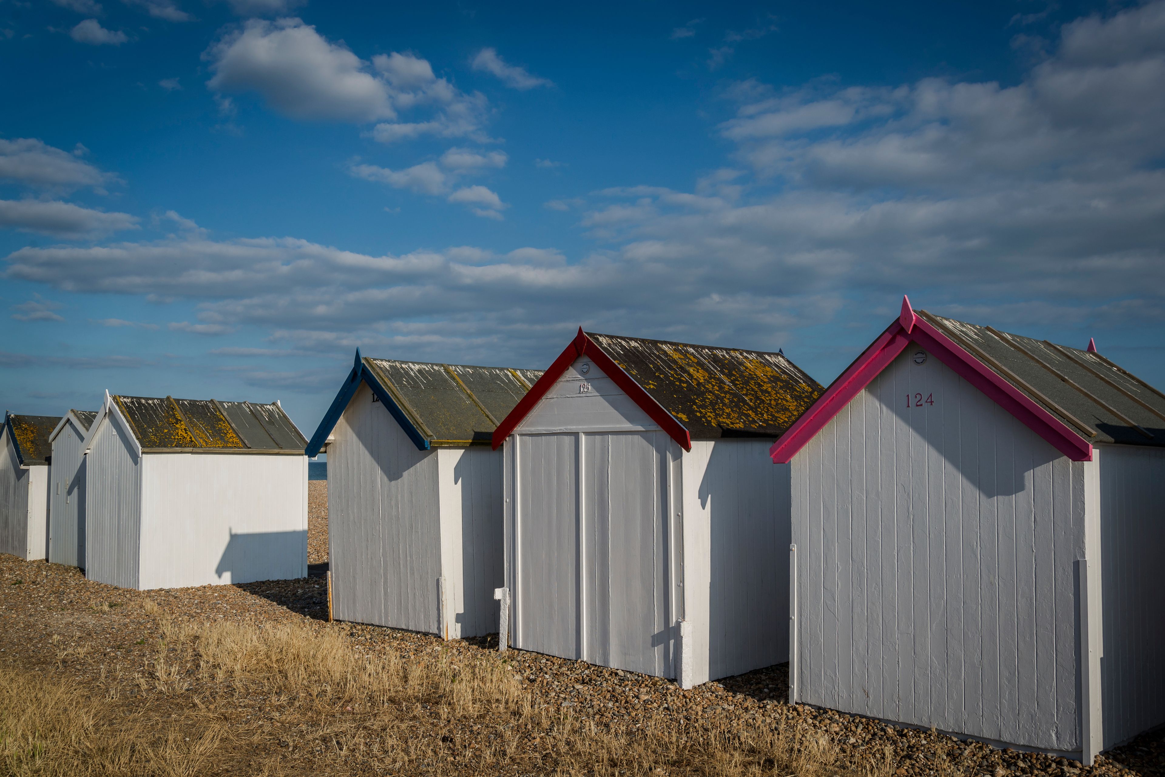A row of beach huts with varying roof colors and numbers.