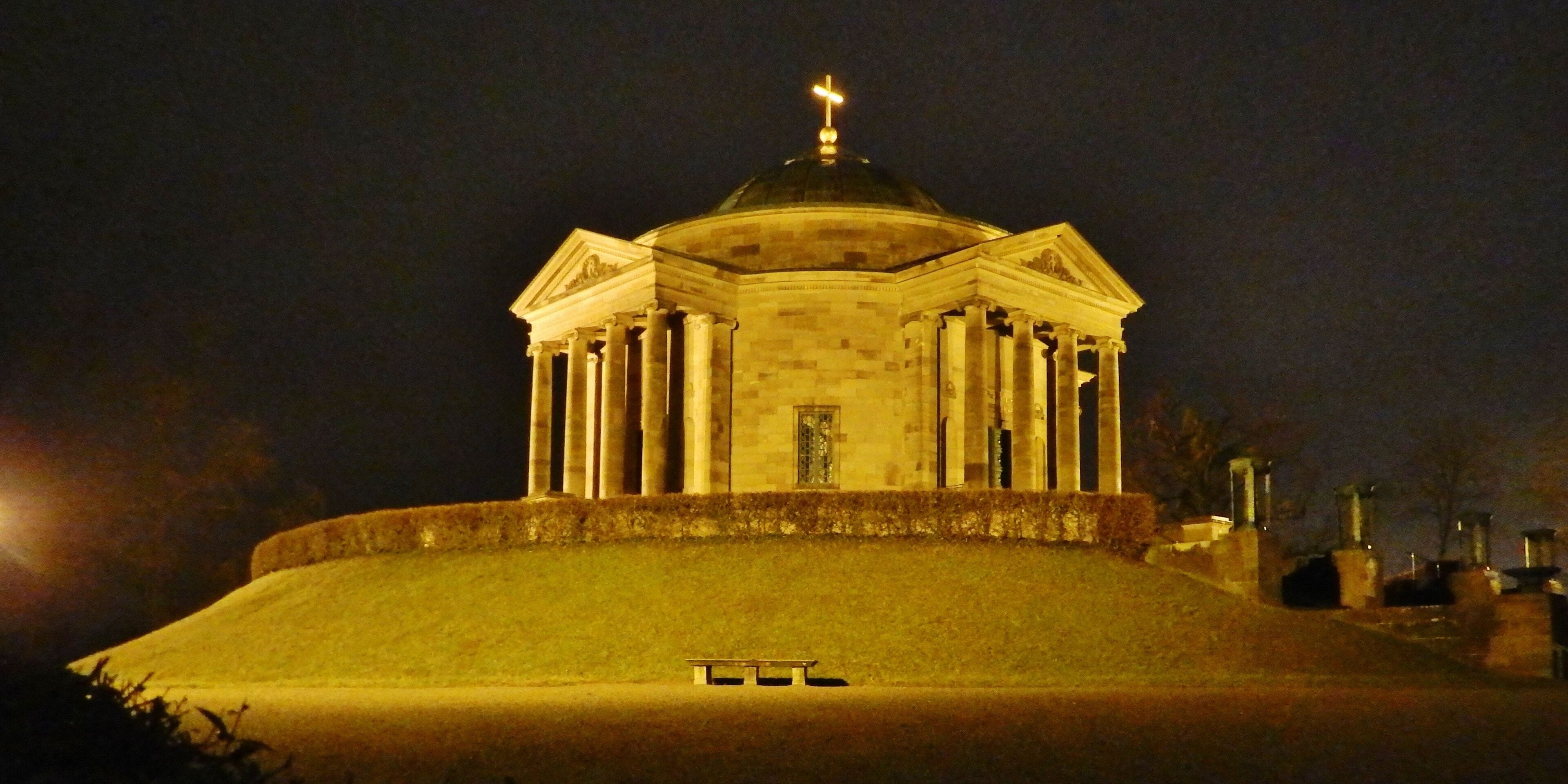 A night-time view of a classical building with a dome and columns, illuminated by artificial lighting.