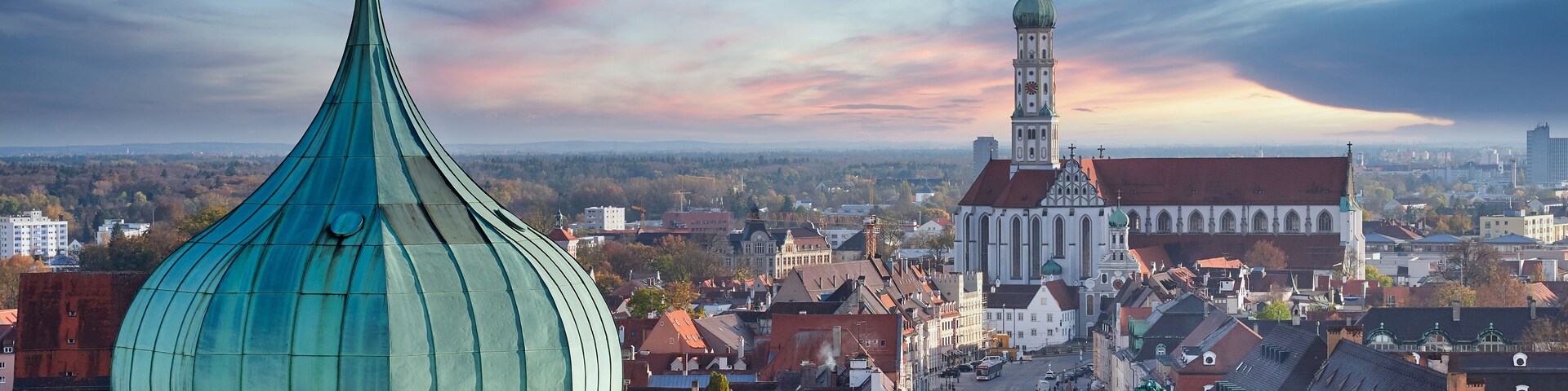 Un paisaje urbano con una cúpula de iglesia de color verde destacada, una iglesia histórica con una torre alta y una zona urbana densa con varios edificios.