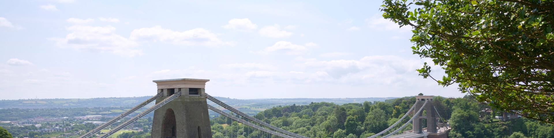 A suspension bridge with a tower, surrounded by lush greenery and a river below.