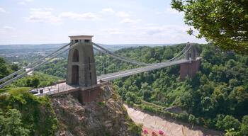A suspension bridge with a tower, surrounded by lush greenery and a river below.