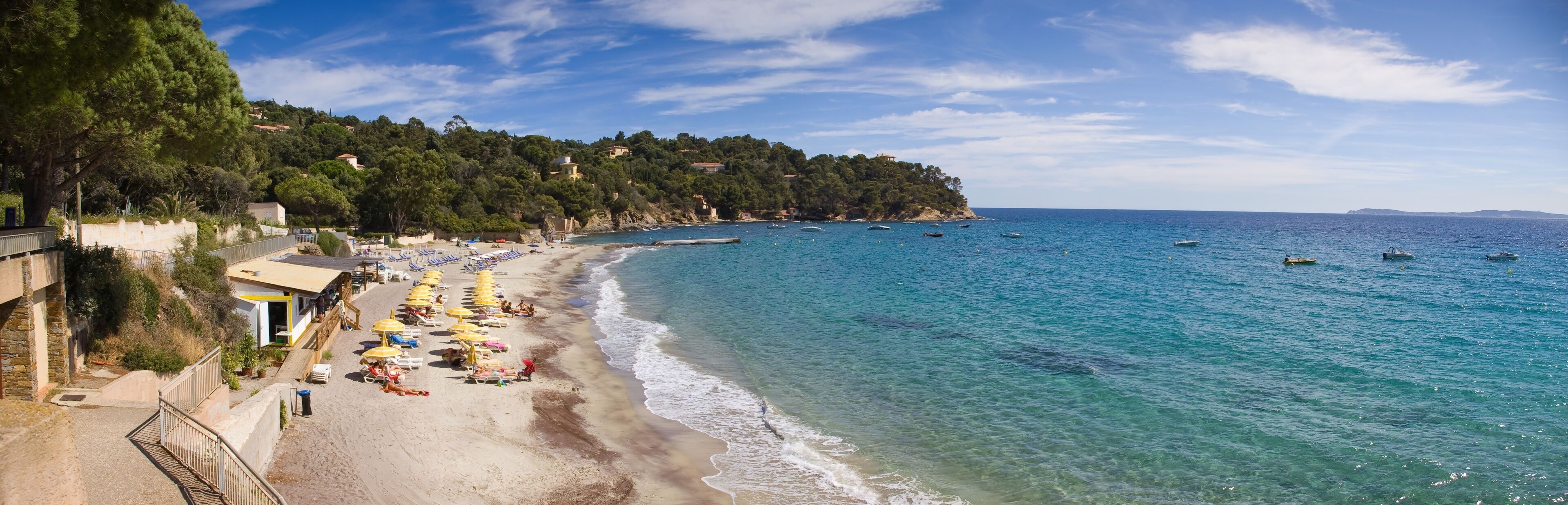 A coastal beach with clear blue waters, sun loungers, and umbrellas.