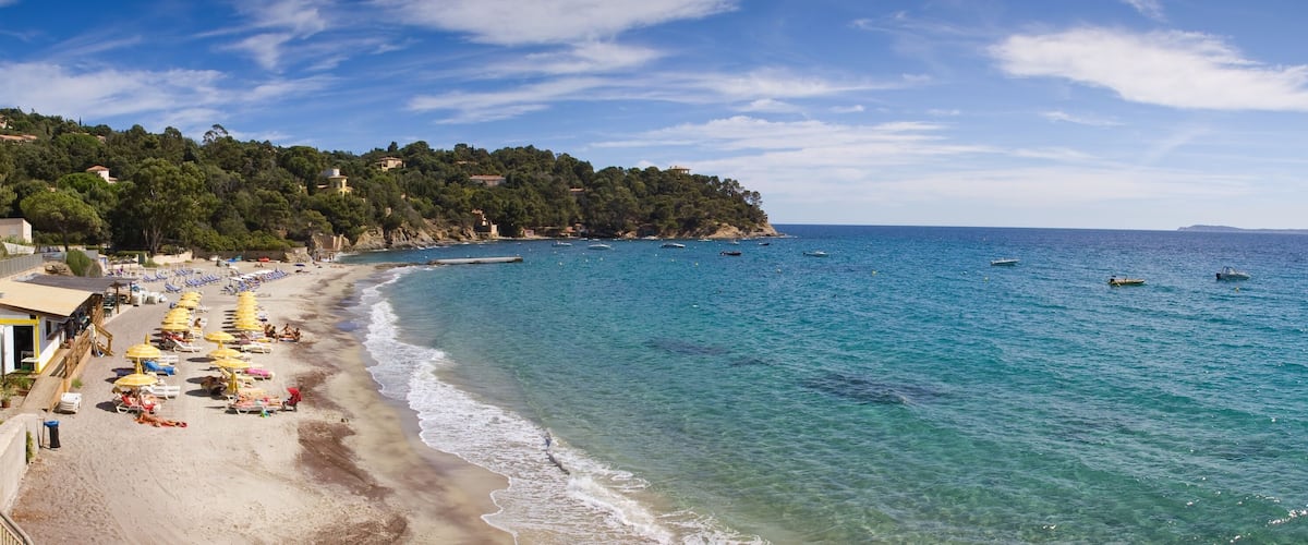 A coastal beach with clear blue waters, sun loungers, and umbrellas.