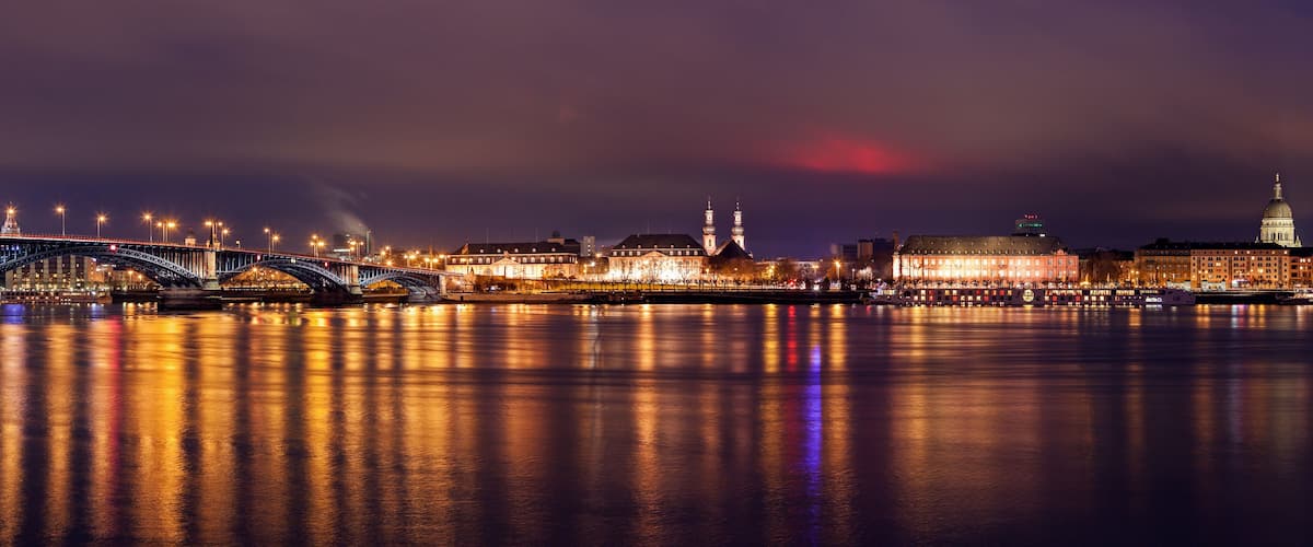 A nighttime cityscape with a bridge, illuminated buildings, and a river reflecting lights.