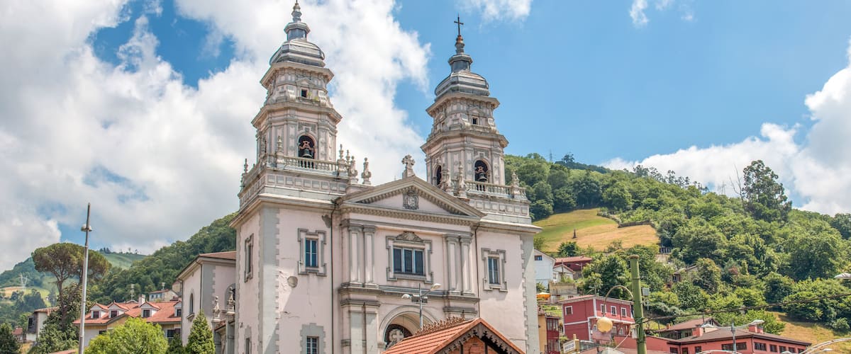 Une église historique dotée de deux tours et d’un dôme, entourée de collines verdoyantes et de bâtiments résidentiels.