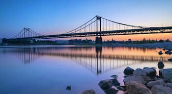A suspension bridge at dusk with a calm river reflecting its structure.