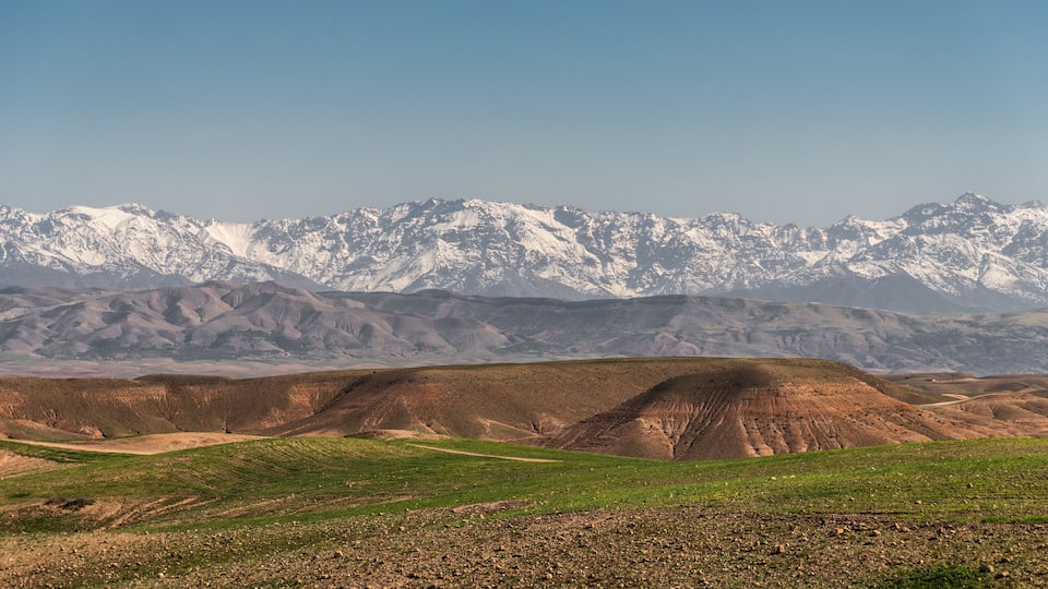 A mountainous landscape with snow-capped peaks and rolling hills in the foreground.