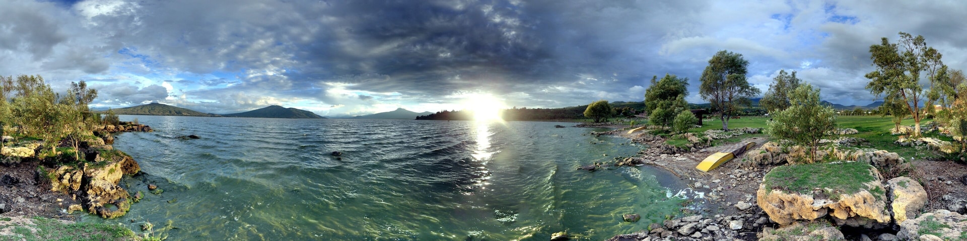 Vista panorámica de un lago con aguas cristalinas, rodeado de costas rocosas y árboles, bajo un cielo nublado.