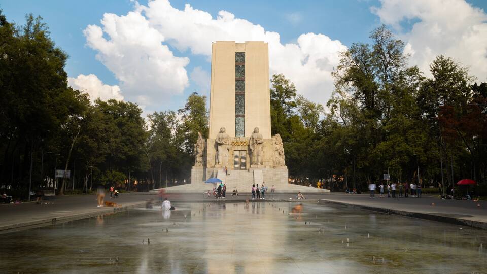 A large monument with a tall central column, surrounded by a reflective water feature and trees.