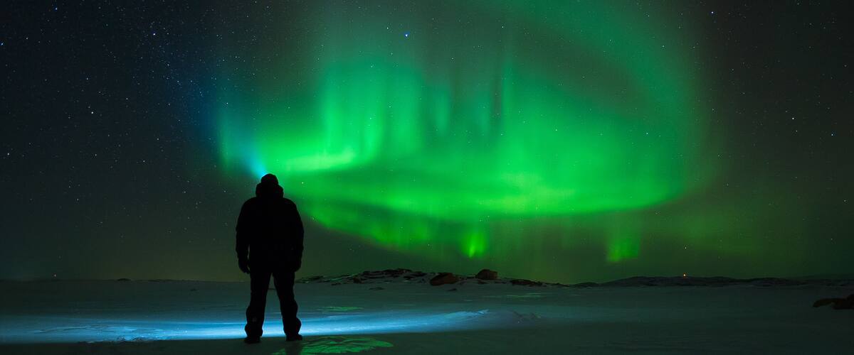A person standing on a snowy landscape under a night sky with green aurora borealis.