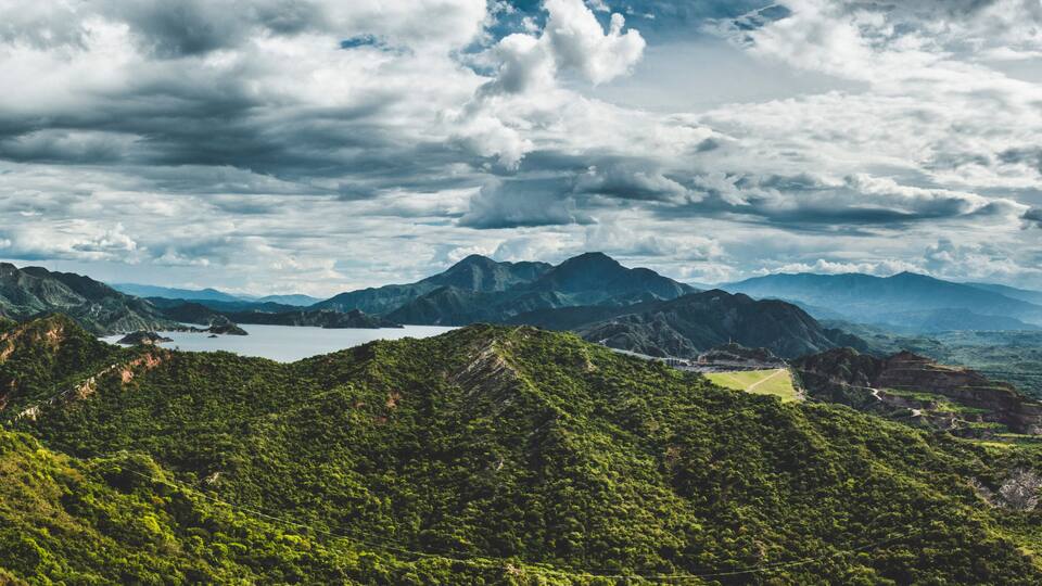 A mountainous landscape with lush greenery, a lake, and a winding road.