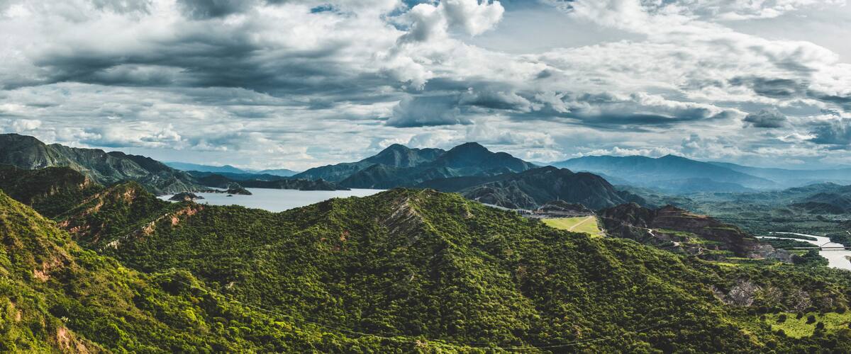 A mountainous landscape with lush greenery, a lake, and a winding road.