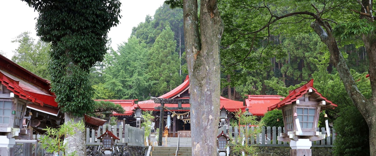 A traditional Japanese temple complex with red-roofed buildings, stone lanterns, and a stone staircase leading up to the entrance.
