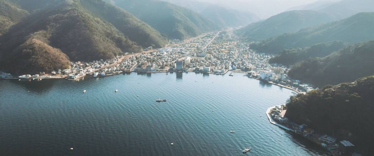 Aerial view of the sprawling cityscape nestled between the shimmering bay and the verdant, misty mountains, Mihama Cape Park, Shizuoka, Japan.