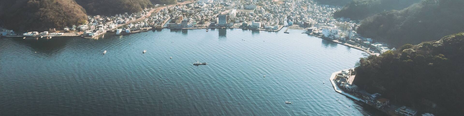 Aerial view of the sprawling cityscape nestled between the shimmering bay and the verdant, misty mountains, Mihama Cape Park, Shizuoka, Japan.