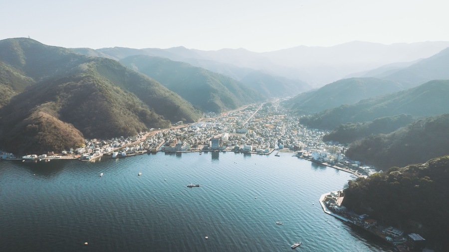 Aerial view of the sprawling cityscape nestled between the shimmering bay and the verdant, misty mountains, Mihama Cape Park, Shizuoka, Japan.