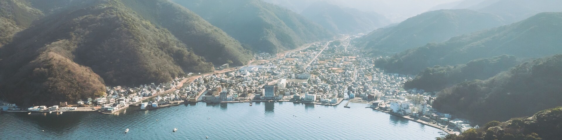 Aerial view of the sprawling cityscape nestled between the shimmering bay and the verdant, misty mountains, Mihama Cape Park, Shizuoka, Japan.