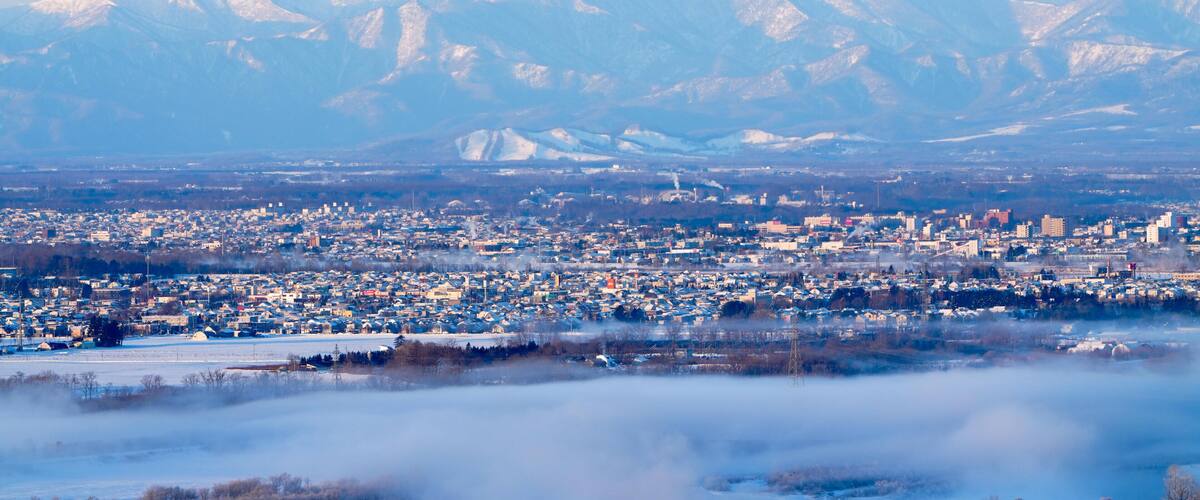A snow-covered mountain range in the background with a cityscape in the foreground.