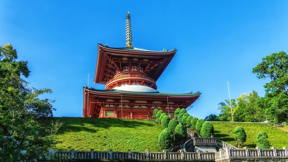 A traditional Japanese pagoda with a multi-tiered roof, surrounded by lush greenery and a stone wall.