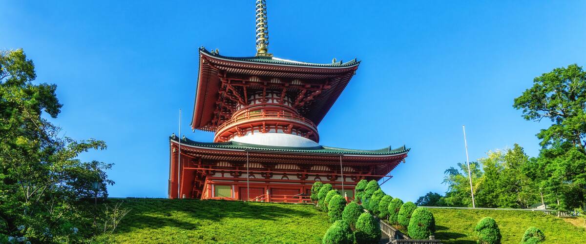 A traditional Japanese pagoda with a multi-tiered roof, surrounded by lush greenery and a stone wall.
