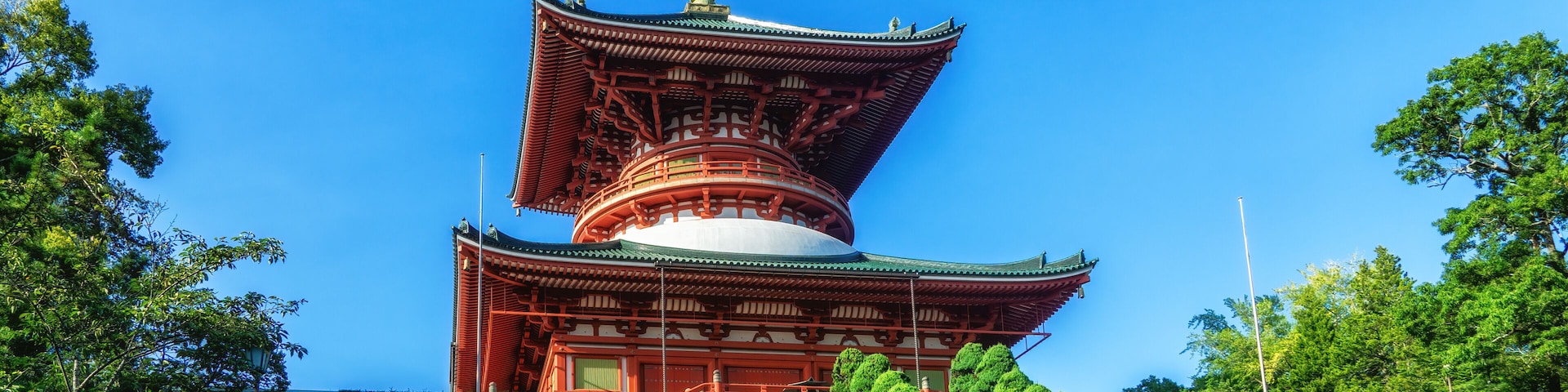 A traditional Japanese pagoda with a multi-tiered roof, surrounded by lush greenery and a stone wall.