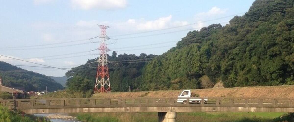 A bridge over a river, a white truck on the bridge, and a red power line tower in the background.
