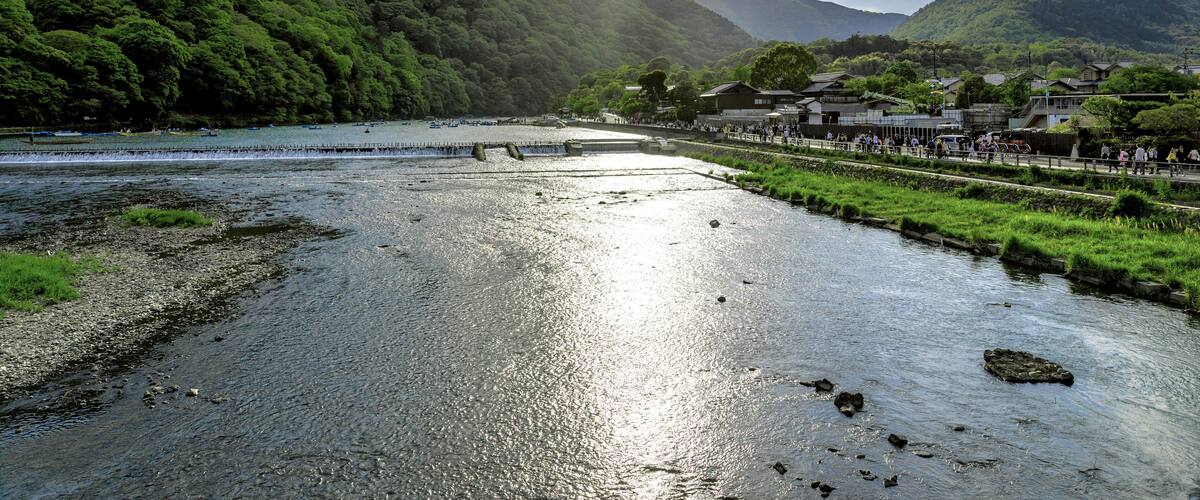 A river with a bridge, lush green hills, and traditional buildings along the riverbank.