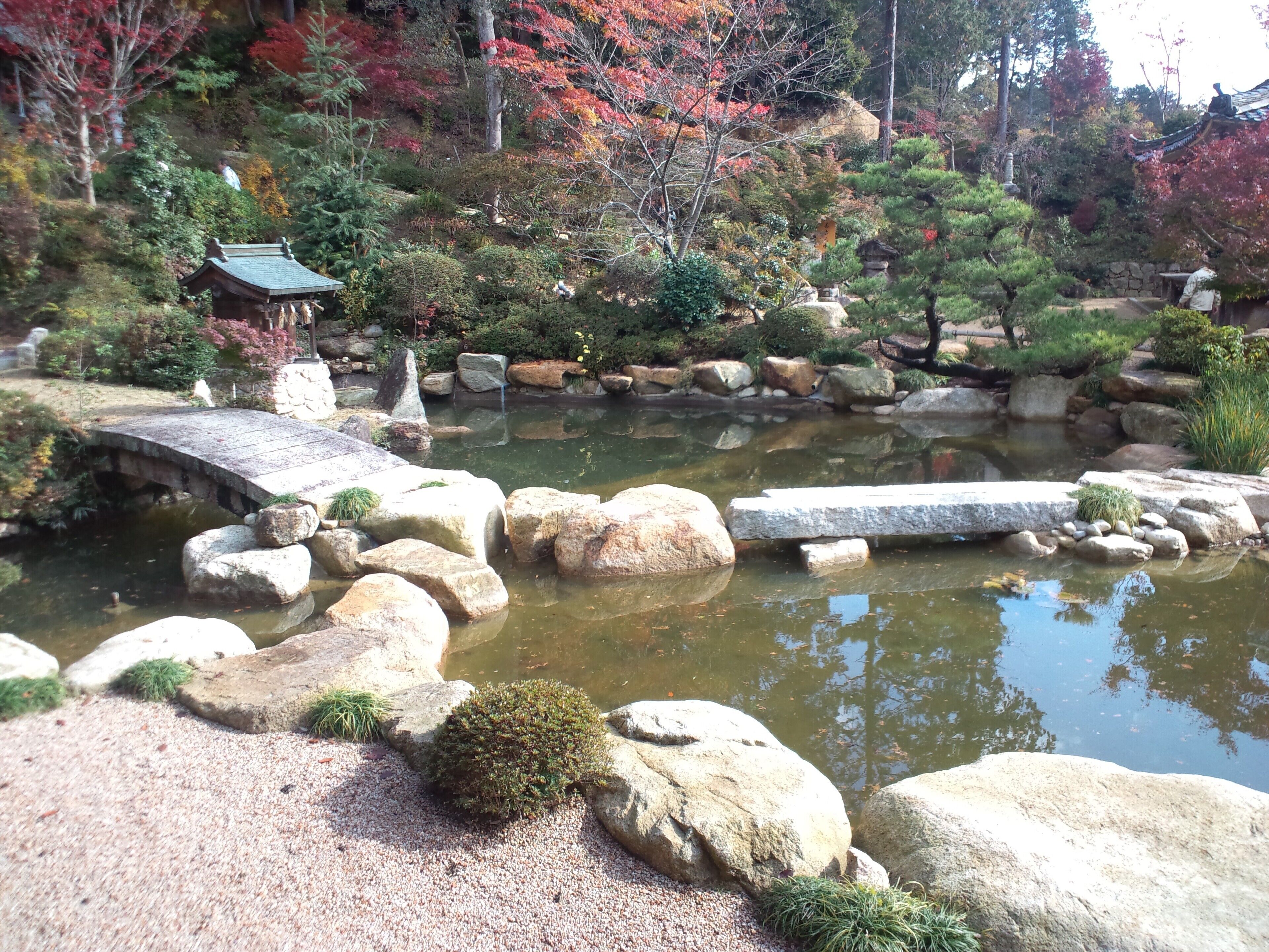 A traditional Japanese garden with a stone bridge, koi pond, and autumn foliage.