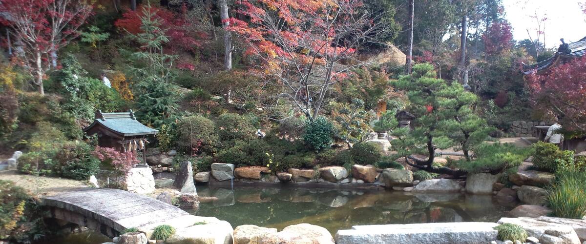 A traditional Japanese garden with a stone bridge, koi pond, and autumn foliage.