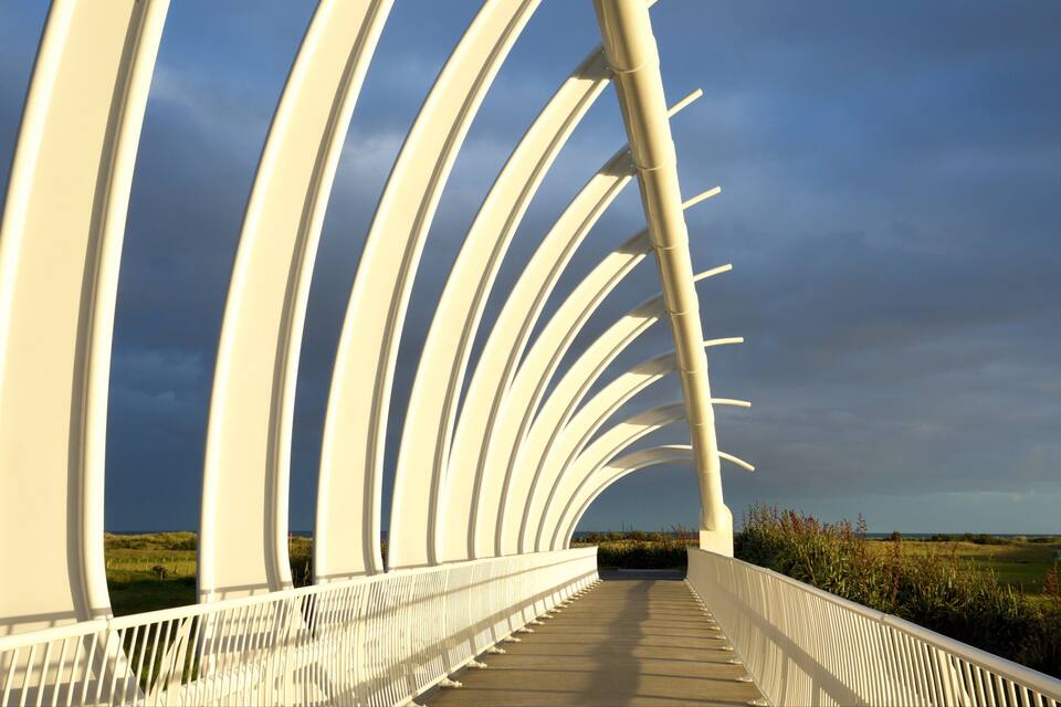 Un pont blanc de disseny corbat amb un cel nuvolós.