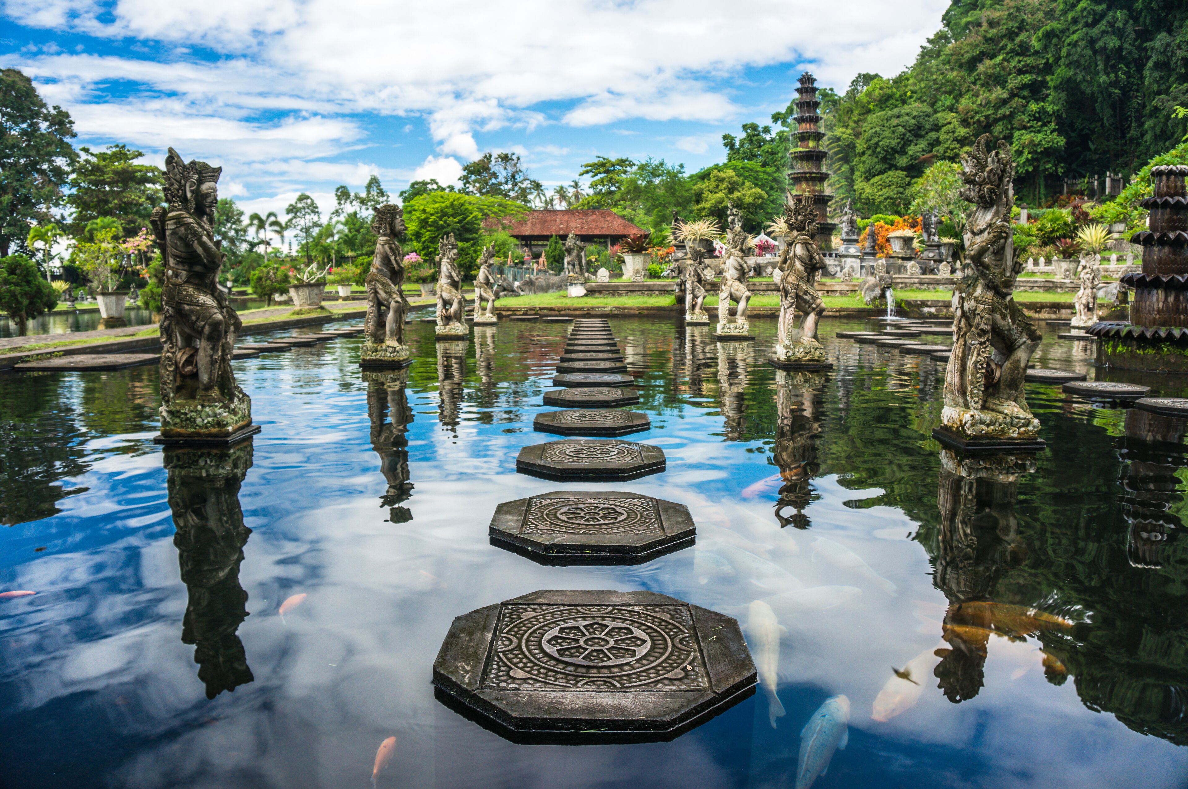 A serene waterway with ornate stone steps leading to a distant pagoda, surrounded by lush greenery and traditional statues.
