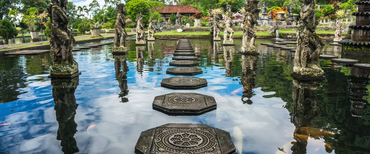 A serene waterway with ornate stone steps leading to a distant pagoda, surrounded by lush greenery and traditional statues.