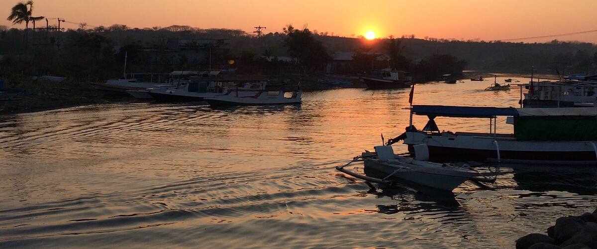 A sunset over a calm river with boats docked along the shore.