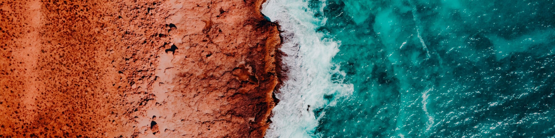 Aerial View of Turquoise Blue Ocean Beach With Crashing Waves and Red Dirt Sand and Rocks