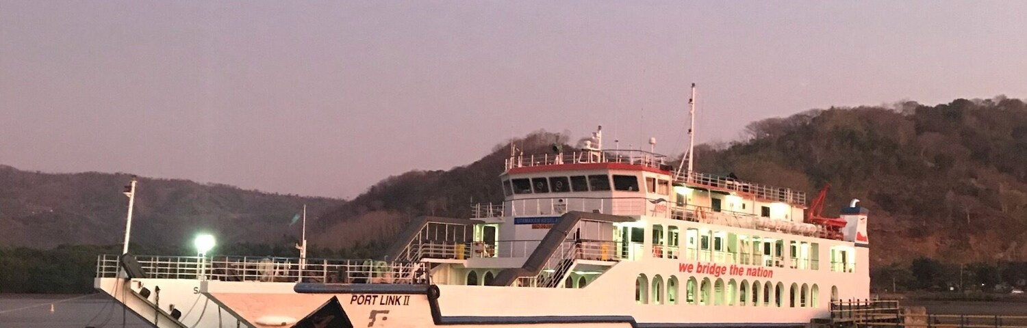 A ferry docked at a pier with a mountainous backdrop.