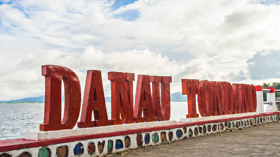 Large red letters spelling "DANAN TONDANO" on a structure by a body of water.
