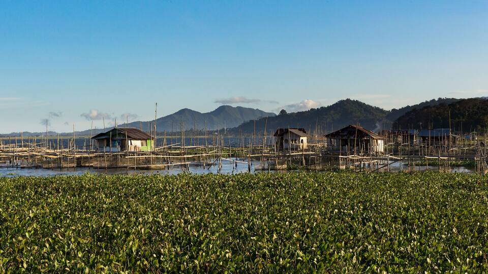 Floating houses on stilts over a water body with a mountainous background.
